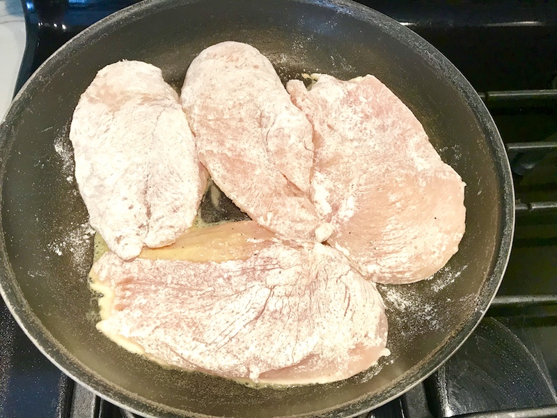 Raw chicken coated in flour cooking in a skillet for Orange Brown Butter Sauce Chicken.