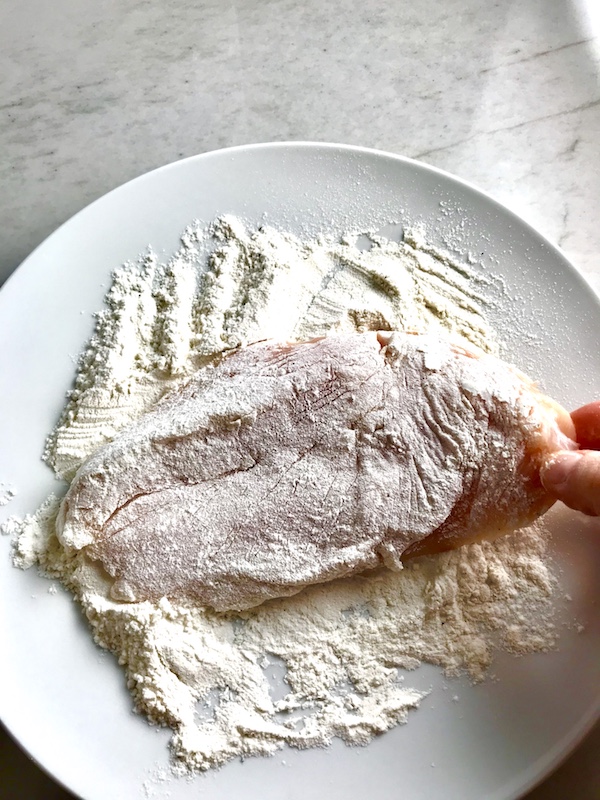 Raw chicken being coated in flour on a plate for Orange Brown Butter Sauce Chicken.