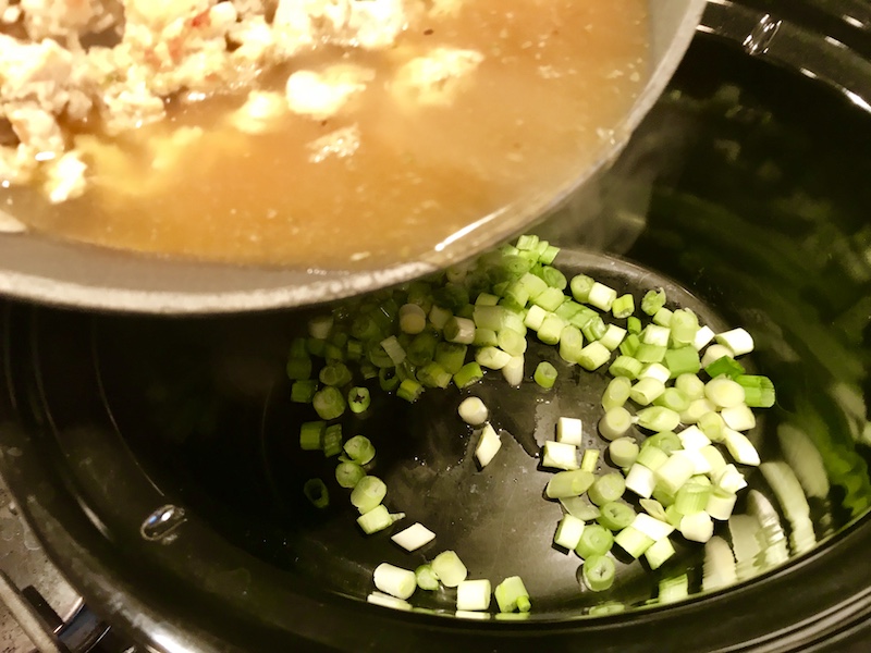 Pan pouring cooked ground chicken and broth into a slow cooker with scallions for Ground Chicken ragu.