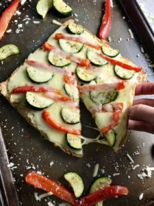 Quinoa Crust Pizza with zucchini and red peppers on pan with slice being pulled out