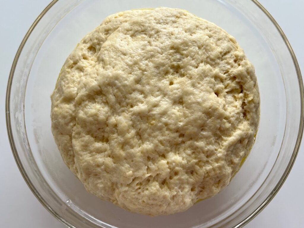 Pizza dough ball doubled in size after 1-2 hours in warm place to rise in a large glass bowl for Chicago Pizza with Chicken Sausage.