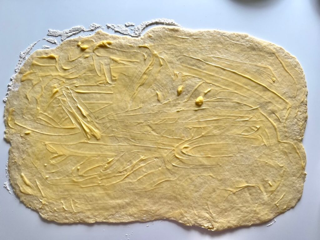 Pizza dough rolled out into a large rectangle and then butter spread all over top for Chicago Pizza with Chicken Sausage.