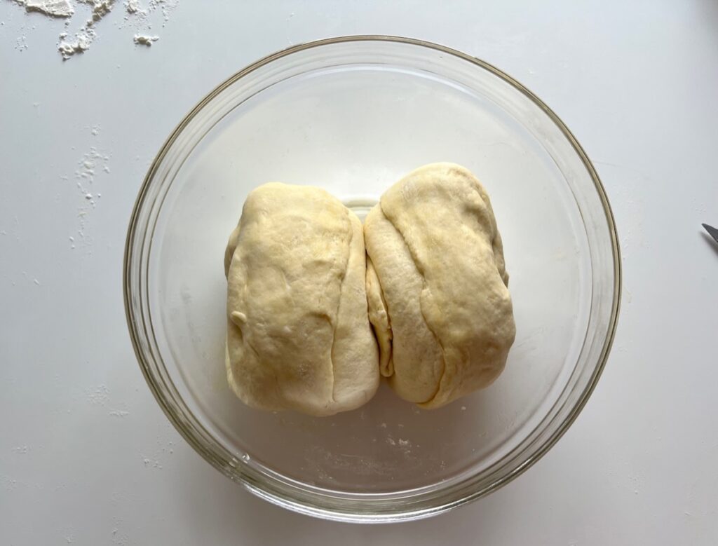 Pizza dough cut into 2 balls in a large glass bowl to rise again in the fridge for Chicago Pizza with Chicken Sausage.