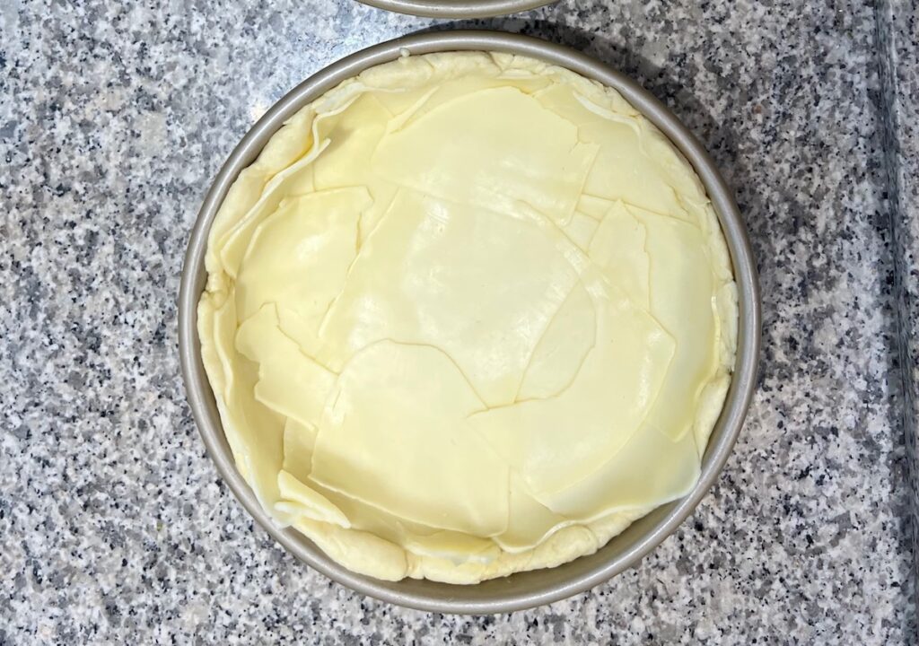 Sliced mozzarella layered over raw pizza dough in a deep dish pan for Chicago Pizza with Chicken Sausage.