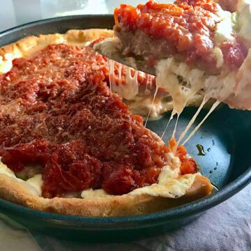 Spatula lifting slice Chicago Style deep dish pizza with chicken sausage and tomatoes on top from a round pan.