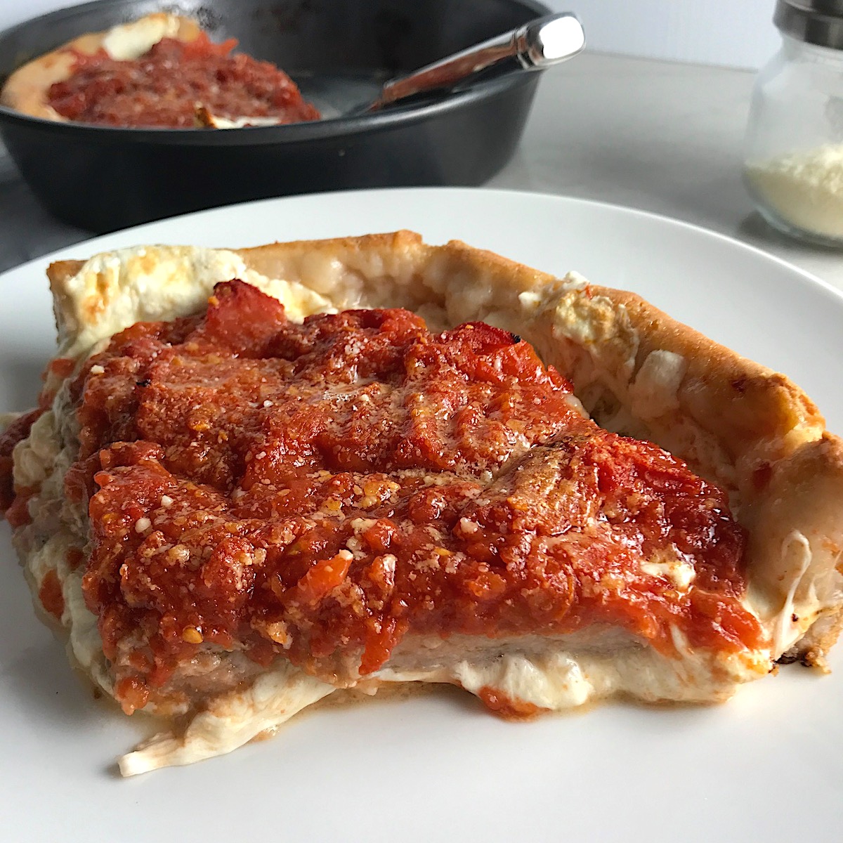 Slice of Chicago Style deep dish pizza with chicken sausage and tomatoes on top on a plate with pizza in pan in background.