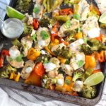 Cilantro Lime Yogurt Sauce for Chicken with Peppers and Broccoli cooked on a sheet pan with sauce drizzled over top and lime wedges on the side.