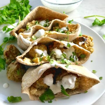 Moroccan Meatball Stuffed Pitas on a plate. They are filled with homemade hummus, moist turkey meatballs made with warm Moroccan spices like ginger, turmeric, and coriander, and then topped with creamy, fresh and bright lemon yogurt sauce.