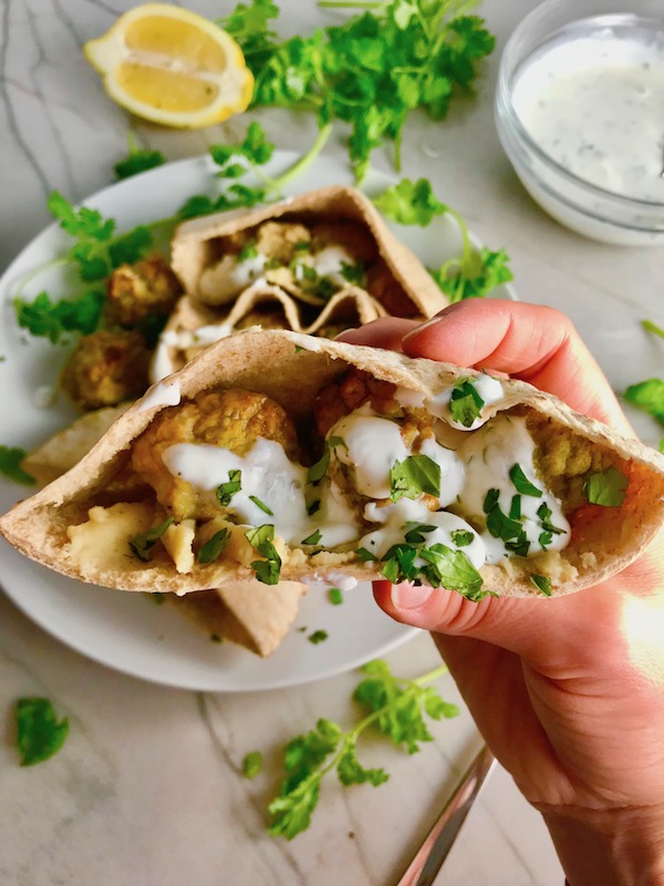Moroccan Meatball Pita Bread Sandwiches Recipe with a hand holding one. They are filled with homemade hummus, moist turkey meatballs made with warm Moroccan spices like ginger, turmeric, and coriander, and then topped with creamy, fresh and bright lemon yogurt sauce.