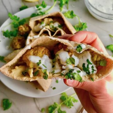 Hand holding Moroccan Pita Bread Sandwiches Recipe on a plate. They are filled with homemade hummus, moist turkey meatballs made with warm Moroccan spices like ginger, turmeric, and coriander, and then topped with creamy, fresh and bright lemon yogurt sauce.