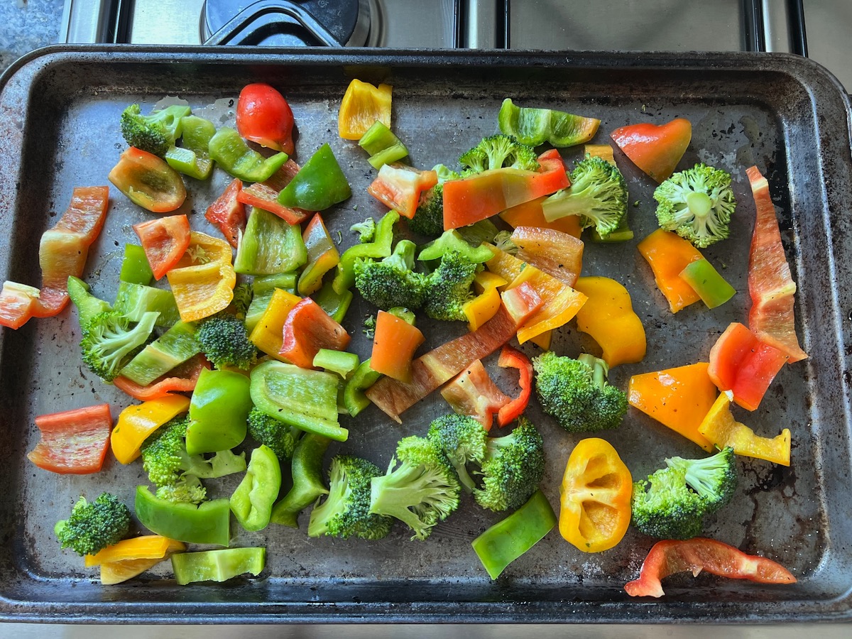 Broccoli florets and cut red, yellow, and green bell peppers on sheet pan before baking for Yogurt Sauce for Chicken with Peppers and Broccoli recipe.
