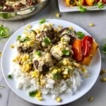 Chipotle Black Bean Recipe Meatballs with corn sauce over rice on white place with peppers on side. Plate on marble counter with peppers on plate in back and pan with meatballs in back.