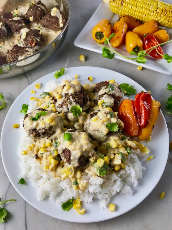 Chipotle Meatballs with corn sauce over rice on white place with peppers on side. Plate on marble counter with peppers on plate in back and pan with meatballs in back.