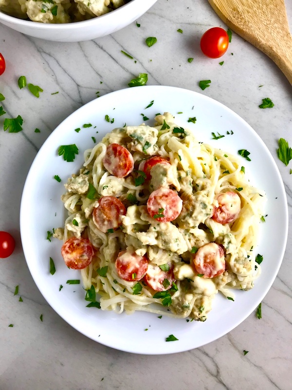 Sausage Cream Noodles with cherry tomatoes on white plate on counter with parsley and tomatoes on plate and counter.