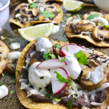 Mushroom and Black Bean Tostadas with Manchego Cheese, and Cilantro Lime Cream are crazy good! The tortillas are baked until crunchy, then topped with homemade refried black beans, nutty aged Manchego Cheese, sautéed mushrooms, and then baked until the cheese is melted. Top with cool cilantro lime cream, crisp radishes, and fresh cilantro. Simple, Gluten-Free, Vegetarian, Delicious!
