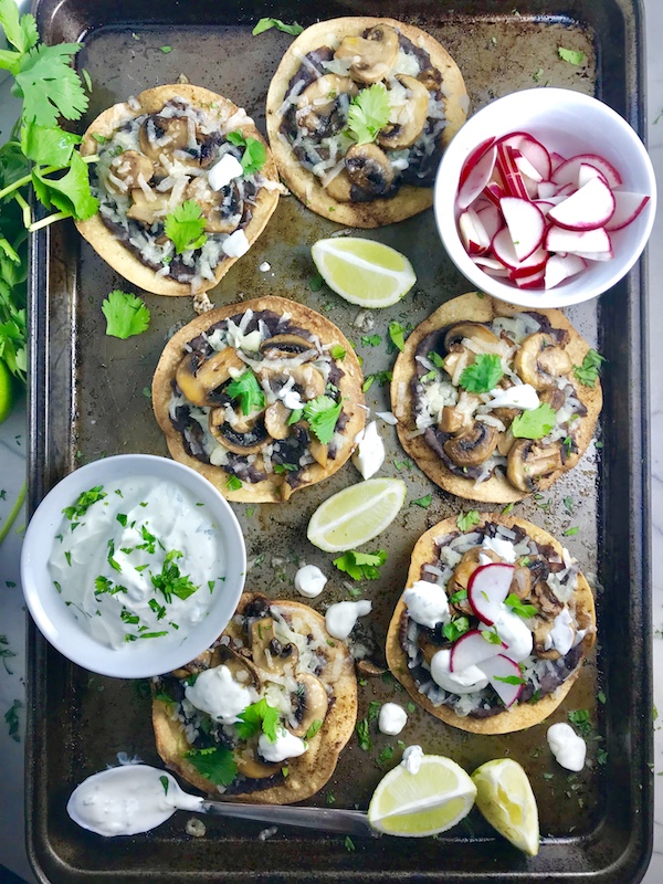 Mushroom and Black Bean Tostadas with Manchego Cheese, and Cilantro Lime Cream are crazy good! The tortillas are baked until crunchy, then topped with homemade refried black beans, nutty aged Manchego Cheese, sautéed mushrooms, and then baked until the cheese is melted. Top with cool cilantro lime cream, crisp radishes, and fresh cilantro. Simple, Gluten-Free, Vegetarian, Delicious!