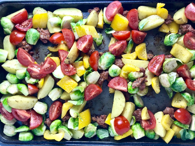 Veggies on pan for One Pan Italian Sausage and Eggs. It's LOADED with flavors and textures. You get the salty Italian Sausage, sweet bell pepper, creamy potatoes, sweet and juicy tomatoes, meaty brussel sprouts, creamy eggs, and salty, nutty cheddar cheese. Best of all, the entire meal cooks on one large pan!