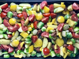 Veggies and raw eggs on pan for One Pan Italian Sausage and Eggs. It's LOADED with flavors and textures. You get the salty Italian Sausage, sweet bell pepper, creamy potatoes, sweet and juicy tomatoes, meaty brussel sprouts, creamy eggs, and salty, nutty cheddar cheese. Best of all, the entire meal cooks on one large pan!