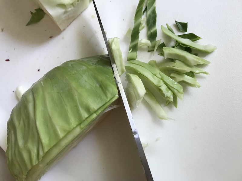 Cabbage being sliced thin on a cutting board for Healthy Chicken Ramen Noodle bowls with flavorful broth, hearty chicken, crunchy veggies, creamy egg, sesame seeds & scallions. Gluten-Free too!