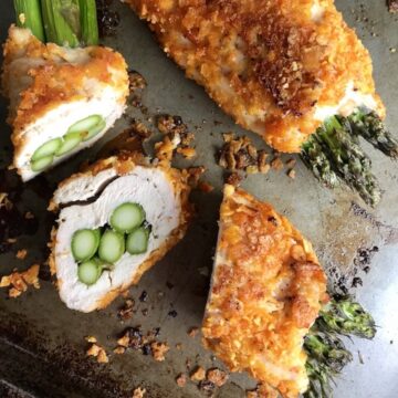 Cheese Tortilla Crusted Chicken Rolls with Asparagus on a sheet pan with one sliced.