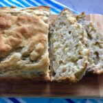 4 Ingredient Banana Bread baked with two slices sliced on wood cutting board. This could not be any EASIER! It is moist, delicious, and so incredibly simple that you can whip it up in 5 minutes, then bake it in the oven.