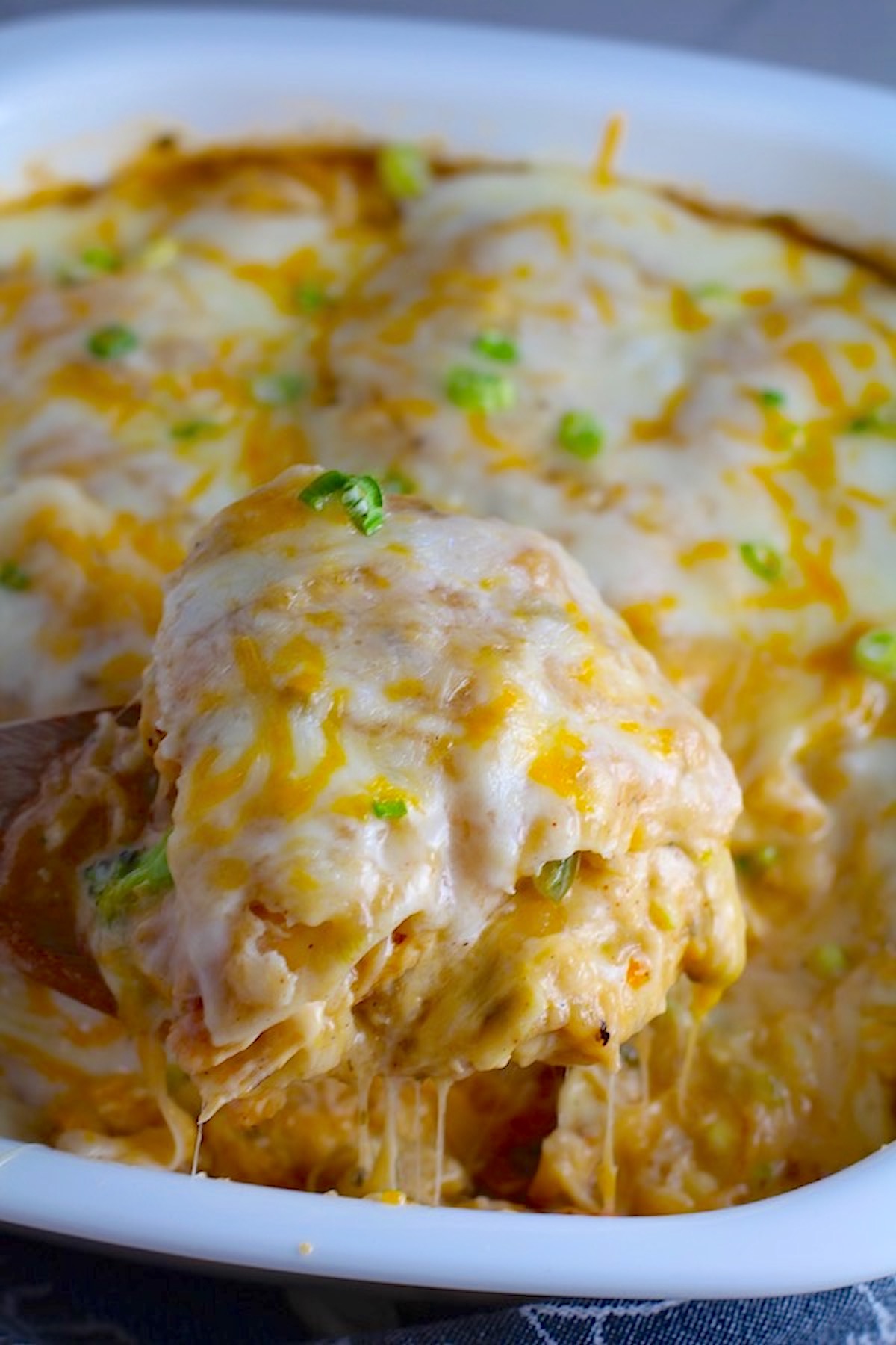 Spatula scooping Sour Cream Chicken Enchilada Casserole with zucchini. It's hearty, cheesy, delicious, & easy because everything is layered in one dish.