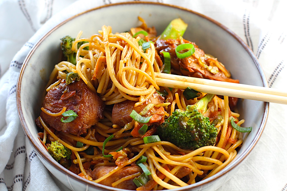 Peanut Teriyaki Chicken & Broccoli with Noodles in a bowl with chopsticks on a towel on table.