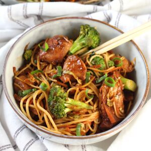 Peanut Teriyaki Chicken & Broccoli with Noodles in a bowl with chopsticks on a towel on table.