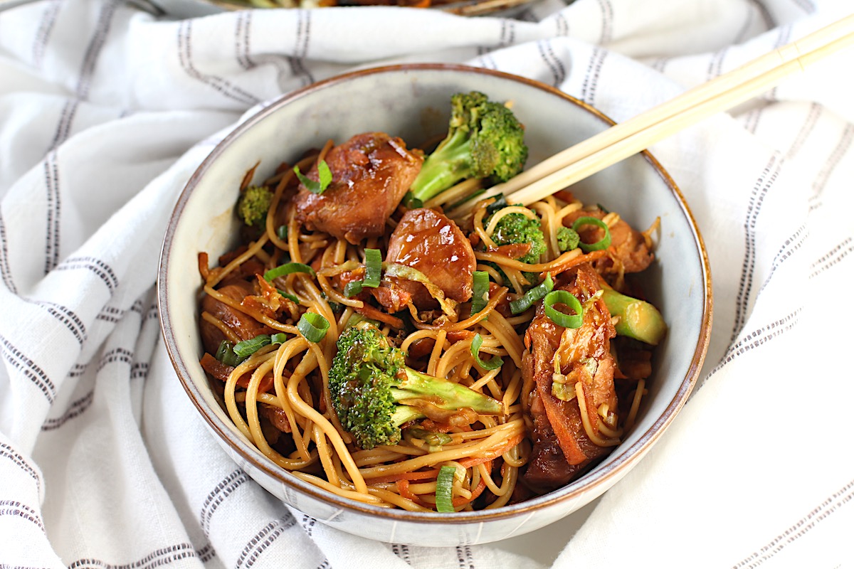 Peanut Teriyaki Chicken & Broccoli with Noodles in a bowl with chopsticks on a towel on table.