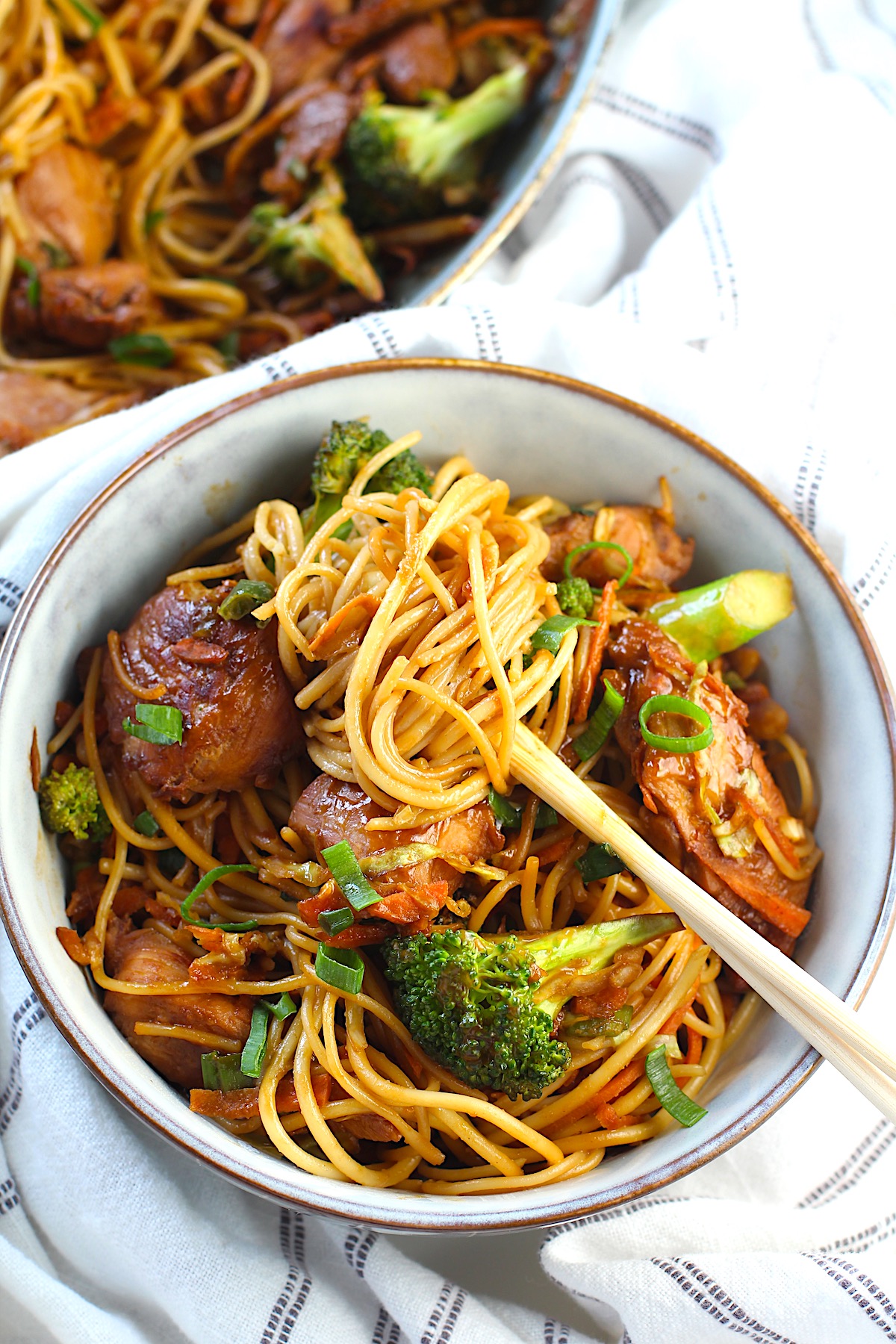 Peanut Teriyaki Chicken & Broccoli with Noodles in a bowl with chopsticks on a towel on table.