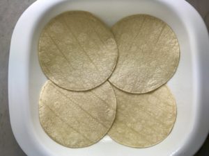 Layer of corn tortillas in pan for Sour Cream Chicken Enchilada Casserole with zucchini. It's hearty, cheesy, delicious, & easy because everything is layered in one dish.