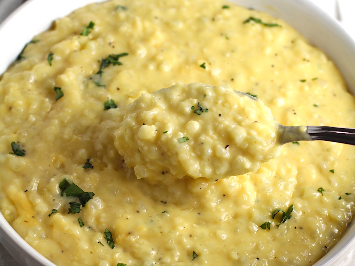 Cheesy Cauliflower Rice with parsley garnish in a bowl with spoon scooping some up. This recipe is so simple with just the flavors from the cauliflower - plus a few other things to help it come together.