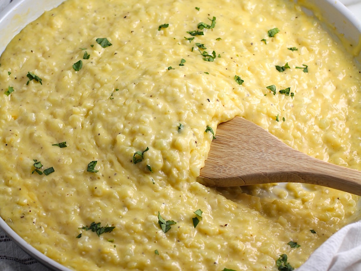 Cheesy Cauliflower Rice with parsley sprinkled on top in a pan with wooden spatula.