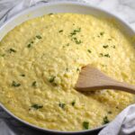 Cheesy Cauliflower Rice with parsley sprinkled on top in a pan with wooden spatula.