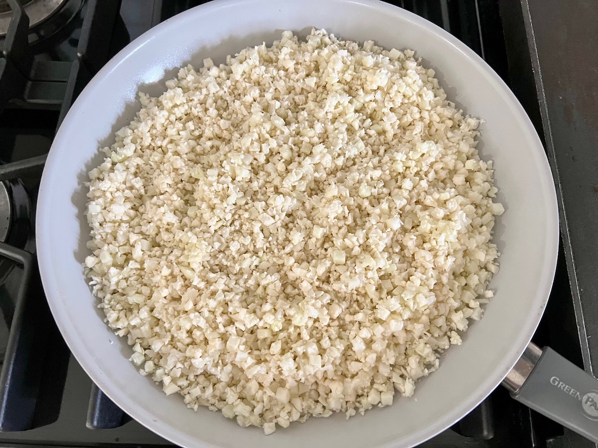 Fresh Riced Cauliflower added to a frying pan to be cooked for Cheesy Cauliflower Rice Recipe.