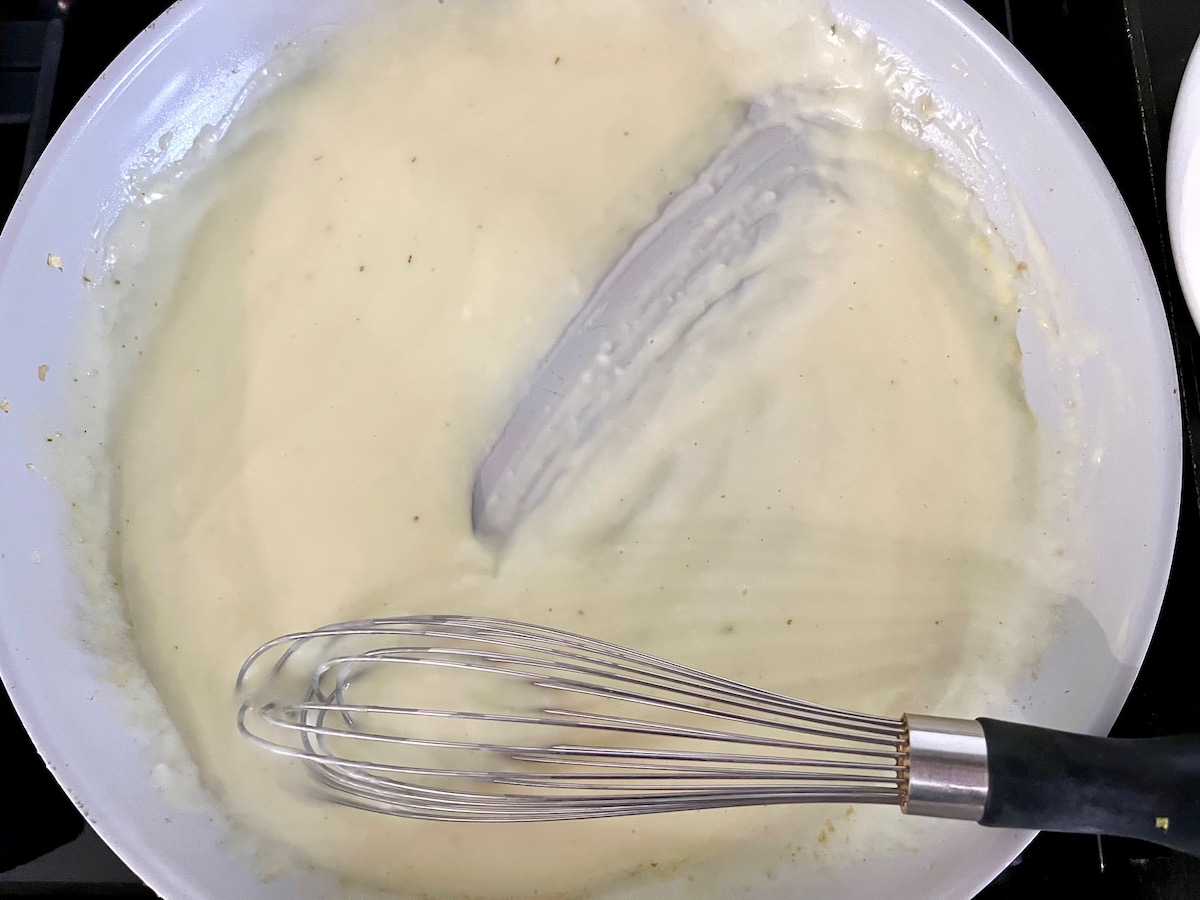 Sauce thickened in a frying pan with a whisk showing track in pack for Cheesy Cauliflower Rice Recipe.