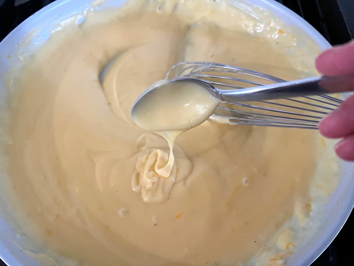 Finished cheese sauce poured from a spoon over the sauce in a frying pan for Cheesy Cauliflower Rice Recipe.