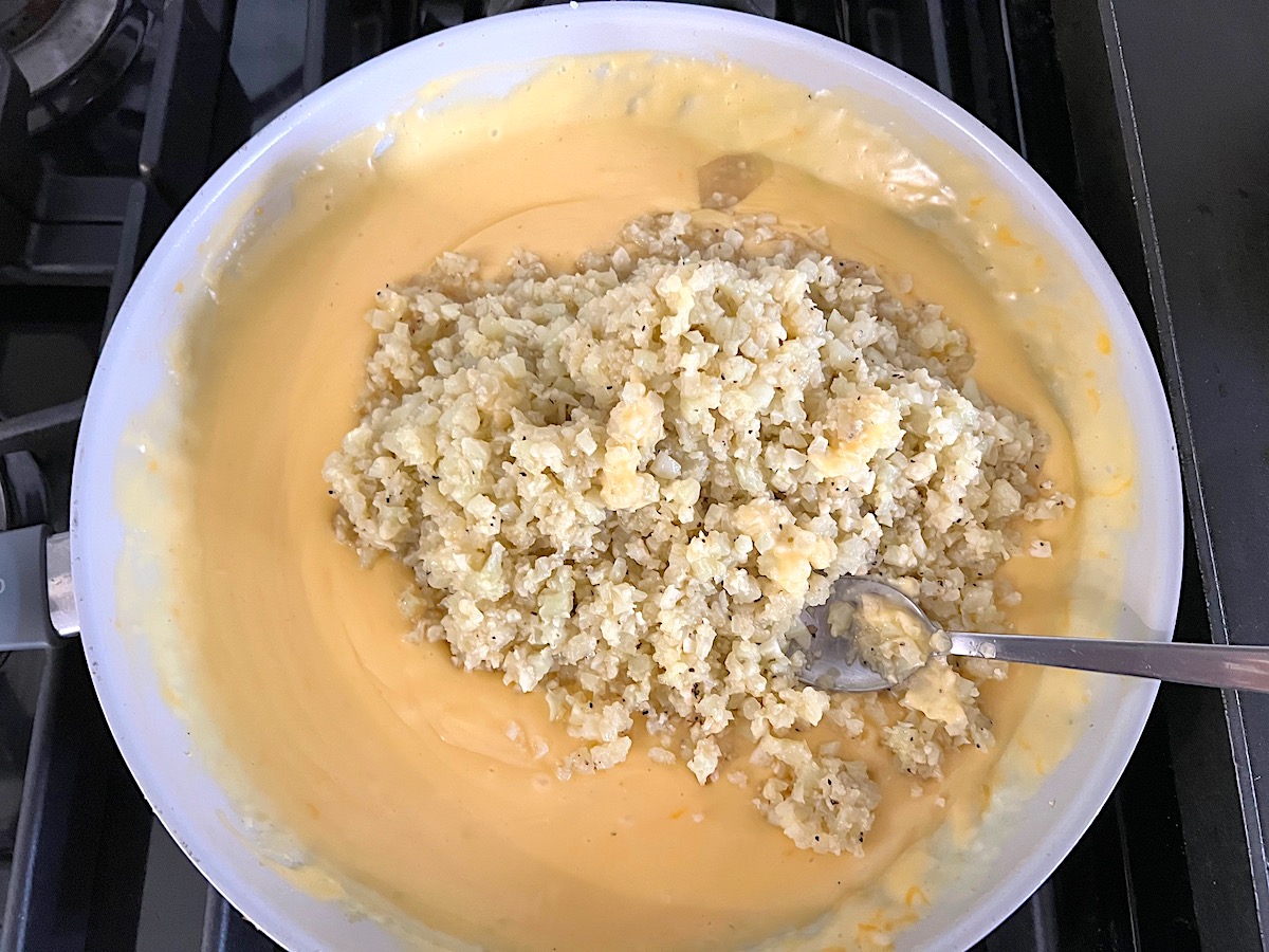 Cooked Cauliflower rice added to the cheese sauce in a frying pan for Cheesy Cauliflower Rice Recipe.