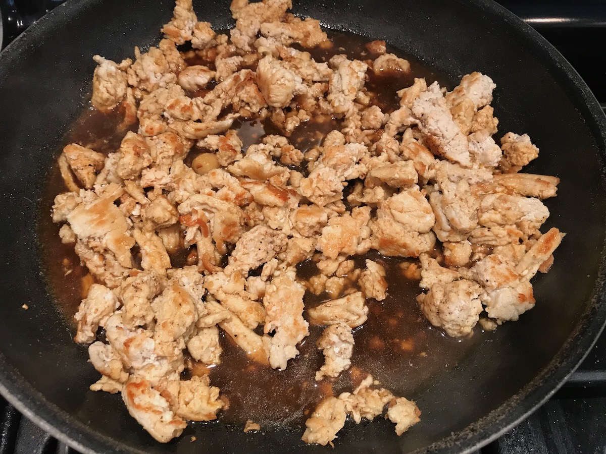 Broth added to ground chicken being seared and browned in a frying pan for the Tomato Chicken Ricotta Pasta recipe.