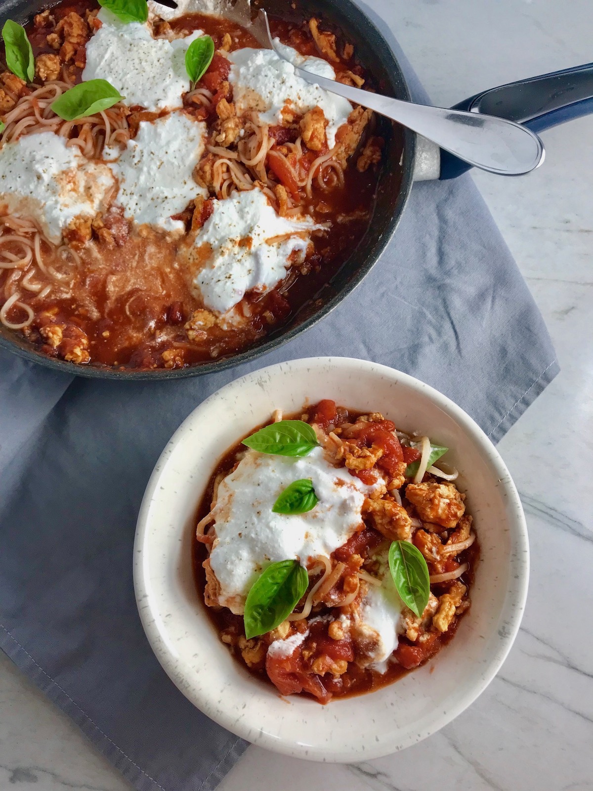 Tomato Chicken Ricotta Pasta in a bowl with fresh basil garnish on counter next to skillet with the rest of the pasta and sauce.