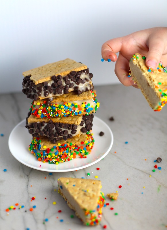 Child's hand taking part of the banana ice cream sandwich away. Banana Ice Cream is literally just 2 ingredients, Frozen Bananas and Almond Milk. Add in crunchy Graham Crackers as the 3rd ingredient and you have a delicious healthy Banana Ice Cream Sandwich! If you have never tried banana ice cream, you are in for a treat! It tastes just like soft serve ice cream.
