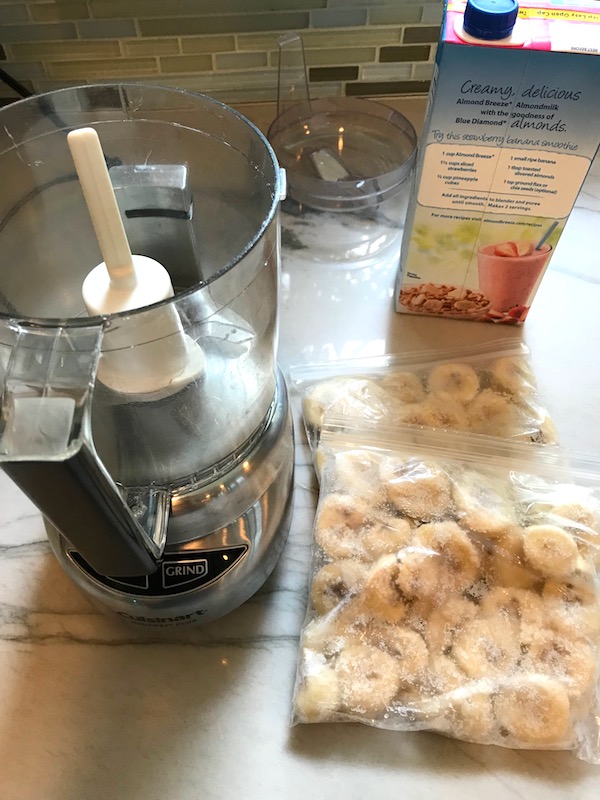 Mini Food Processor on counter with frozen bananas in baggies and almond milk carton. Banana Ice Cream is literally just 2 ingredients, Frozen Bananas and Almond Milk. Add in crunchy Graham Crackers as the 3rd ingredient and you have a delicious healthy Banana Ice Cream Sandwich! If you have never tried banana ice cream, you are in for a treat! It tastes just like soft serve ice cream.