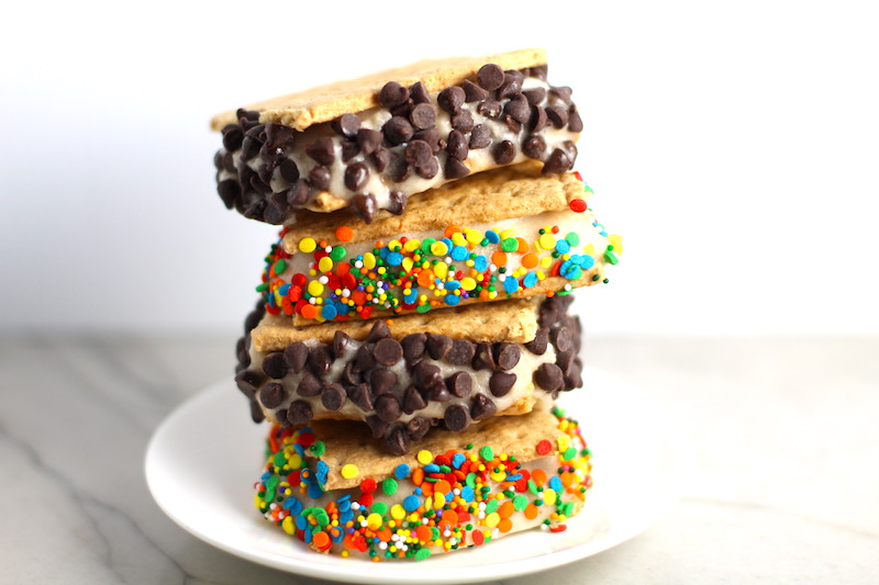 Banana Ice Cream sandwiches with graham crackers, sprinkles, and chocolate chips stacked on plate on counter. Banana Ice Cream is literally just 2 ingredients, Frozen Bananas and Almond Milk. Add in crunchy Graham Crackers as the 3rd ingredient and you have a delicious healthy Banana Ice Cream Sandwich! If you have never tried banana ice cream, you are in for a treat! It tastes just like soft serve ice cream.