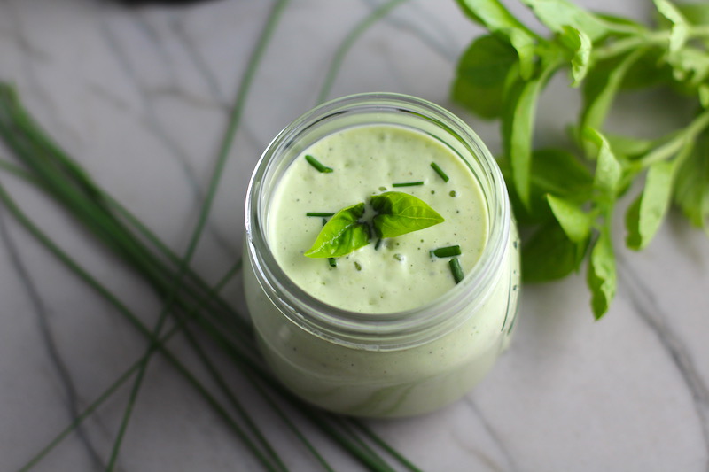 Basil & Chive Yogurt Dressing in a jar on counter with basil leaves and chives on top and on the counter. This dressing with Lemon and Honey is creamy, light, savory, and a little bit sweet. It takes only minutes to make this delicious homemade dressing. Basil & Chive Yogurt Dressing is perfect for salads, for drizzling over roasted veggies, steak, chicken, or fish, and amazing for dipping fries into!!