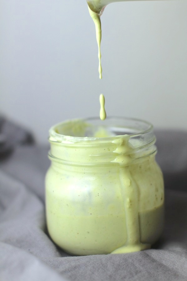 Basil & Chive Yogurt Dressing dripping into a jar sitting on a gray napkin. This dressing with Lemon and Honey is creamy, light, savory, and a little bit sweet. It takes only minutes to make this delicious homemade dressing. Basil & Chive Yogurt Dressing is perfect for salads, for drizzling over roasted veggies, steak, chicken, or fish, and amazing for dipping fries into!!