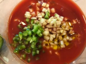 Green pepper, cucumber, garlic, scallions, red pepper, and tomato juice in a bowl for Roasted Red Pepper Gazpacho recipe from talkingmeals.com