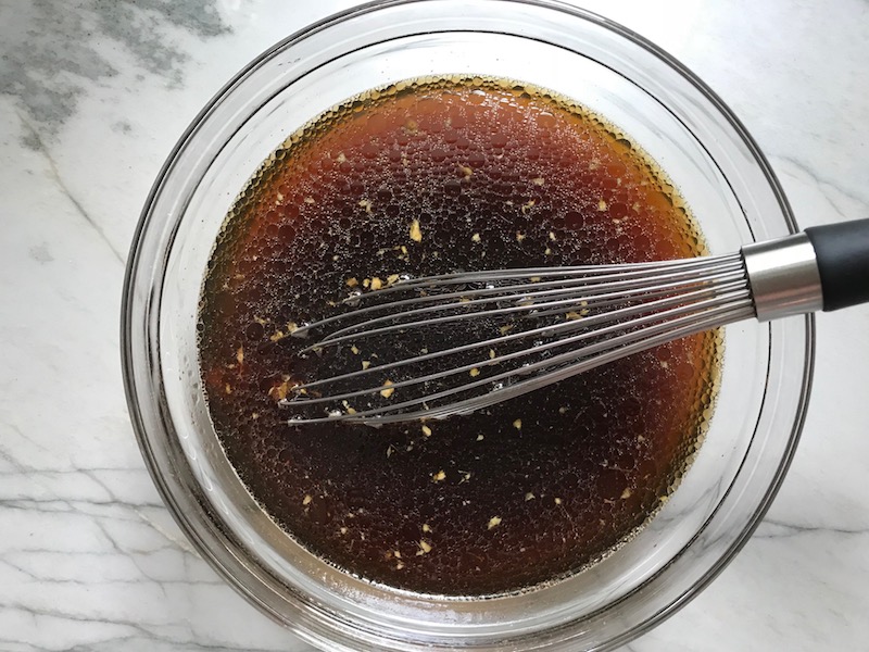 Sauce in clear bowl with whisk for Korean Rice Bowl with Lentils and Cauliflower recipe, which is da bomb, exploding with flavor! The rice soaks up the sauce, which gives you a nutty, salty flavor from sesame oil and soy sauce, a warm and zesty kick from ginger and garlic, and sweetness from honey to balance it all out. Lentils and cauliflower give a meaty bite.
