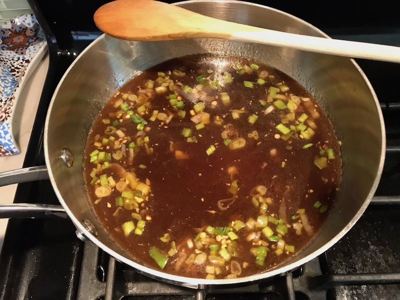 Sauce in pot with wood spoon on stove for Korean Rice Bowl with Lentils and Cauliflower recipe, which is da bomb, exploding with flavor! The rice soaks up the sauce, which gives you a nutty, salty flavor from sesame oil and soy sauce, a warm and zesty kick from ginger and garlic, and sweetness from honey to balance it all out. Lentils and cauliflower give a meaty bite.