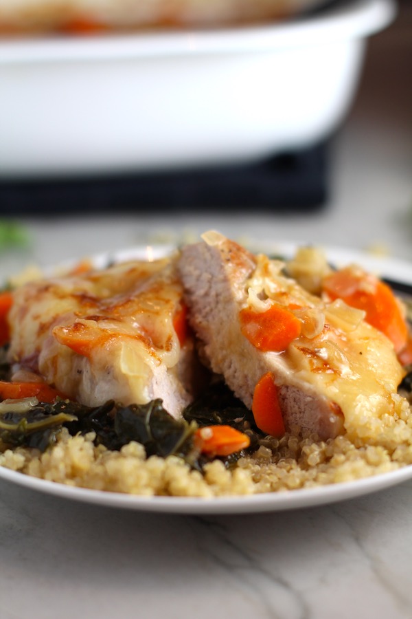 Close up of Smothered Pork Chop cut in half on quinoa with carrots and kale. This Smothered Pork Chops with vegetables recipe is a true midwestern comfort dish with layers of vegetables and meaty pork chops smothered in a creamy sauce and cheese. The pork chops in this delicious casserole are left whole so that you get an entire portion dripping in goodness in one scoop.
