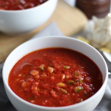 This Roast Red Pepper Gazpacho recipe is Summer in a bowl. It's cool, tangy, crunchy, fresh, and creamy. The base is tomato, but this Gazpacho recipe puts Roast Red Pepper in the starring role, which brings another layer of creamy sweetness. Then you get the crunch from the green pepper, cucumber, garlic and scallions.